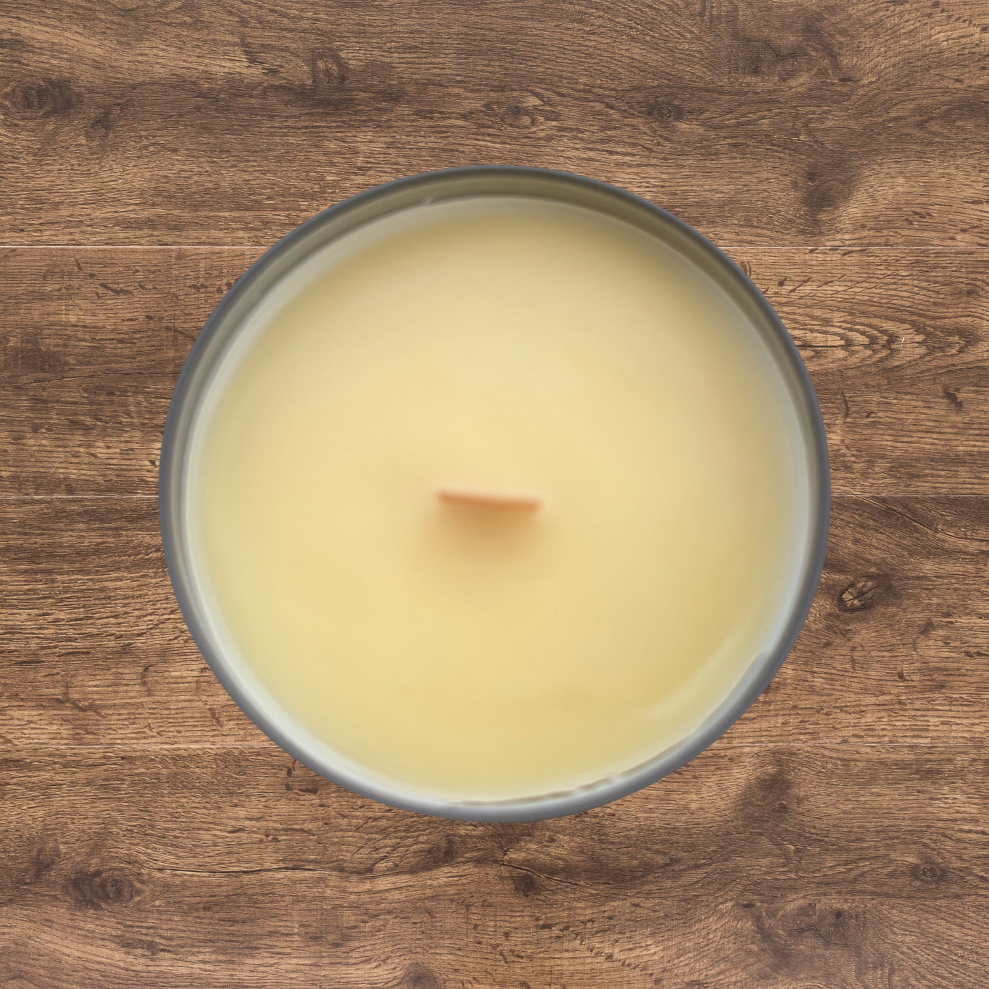 top-down view of a hand-poured beeswax candle with a natural golden surface and a centered wooden wick. Set in a clear glass container. Simple, traditional presentation with a raw, handmade look.